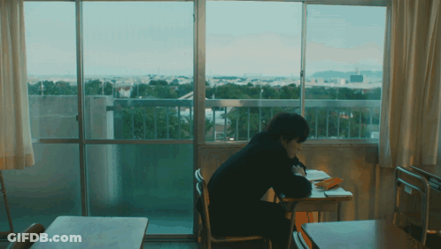 A Person Is Sitting At A Desk In Front Of A Window GIF