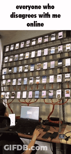 A Person Is Sitting At A Desk With A Laptop In Front Of A Wall Full Of Cell Phones GIF