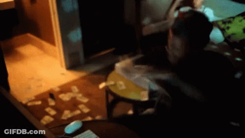 A Person Is Sitting At A Table With Cards On The Floor In A Dark Room GIF