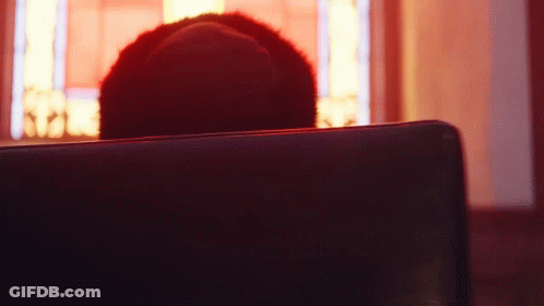 A Person Is Sitting In A Dark Room With A Red Light Behind Them GIF