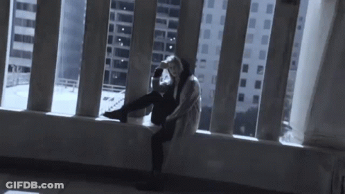 A Person Is Sitting On A Balcony Looking Out A Window At A City . GIF