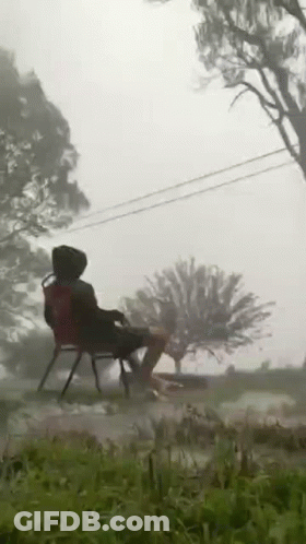 A Person Is Sitting On A Chair In The Grass In A Field . GIF