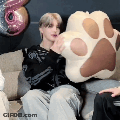 A Person Is Sitting On A Couch Holding A Paw Pillow GIF