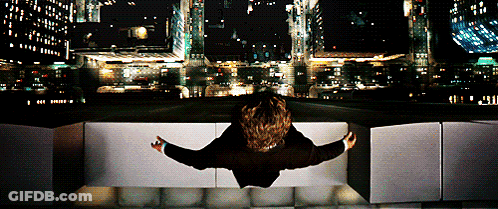 A Person Is Sitting On A Ledge Looking Out Over A City At Night GIF