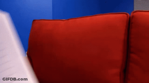 A Person Is Sitting On A Red Couch Holding A Piece Of Paper GIF