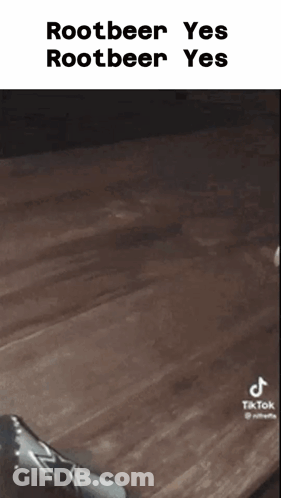 A Person Is Sitting On A Wooden Table With A Bottle Of Rootbeer In Front Of Them . GIF