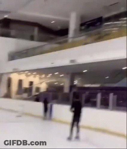 A Person Is Skating On An Ice Rink In A Large Building GIF