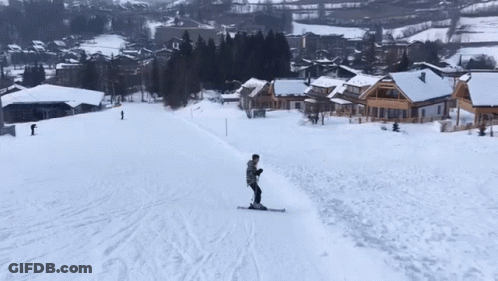 A Person Is Skiing Down A Snow Covered Slope With Houses In The Background GIF