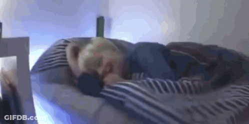 A Person Is Sleeping On A Bed With A Striped Blanket . GIF