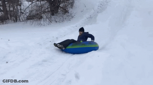 A Person Is Sliding Down A Snowy Hill On A Blue And Green Tube GIF