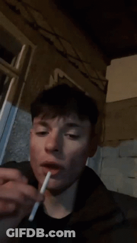 A Person Is Smoking A Cigarette In Front Of A Wall With A Floral Design On It GIF