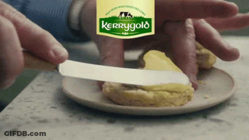 A Person Is Spreading Butter On A Biscuit With A Label For Kerrygold In The Background GIF