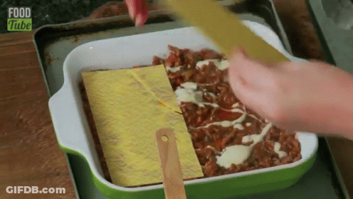 A Person Is Spreading Cheese On Top Of A Casserole Dish With Food Tube Written On The Bottom . GIF