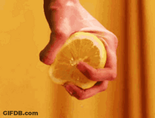 A Person Is Squeezing A Slice Of Lemon In Their Hand . GIF