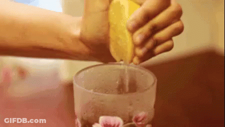 A Person Is Squeezing Lemon Juice Into A Glass . GIF