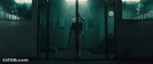 A Person Is Standing In A Dark Room Behind A Glass Door Holding A Knife . GIF