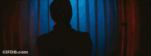 A Person Is Standing In A Dark Room In Front Of A Blue And Red Curtain . GIF