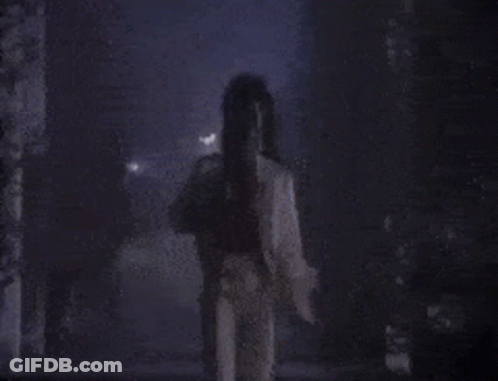A Person Is Standing In A Dark Room With A Purple Background . GIF