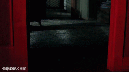A Person Is Standing In A Dark Room With A Red Curtain . GIF
