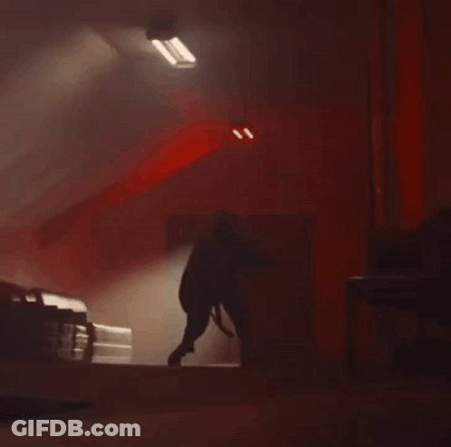 A Person Is Standing In A Dark Room With A Red Light On The Ceiling . GIF