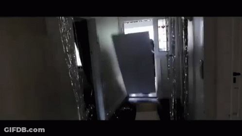 A Person Is Standing In A Hallway Carrying A Large Piece Of Furniture . GIF