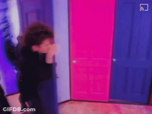 A Person Is Standing In A Room With Pink And Blue Doors And Covering Their Face . GIF