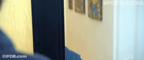 A Person Is Standing In Front Of A Door With A Painting On The Wall Behind Them . GIF