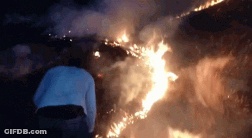 A Person Is Standing In Front Of A Fire At Night . GIF