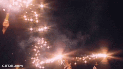 A Person Is Standing In Front Of A Fireworks Display With The Letter S On The Bottom Right Corner . GIF