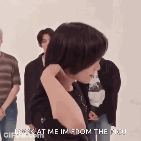 A Person Is Standing In Front Of A Group Of People And Holding Their Hair In Front Of Their Face . GIF