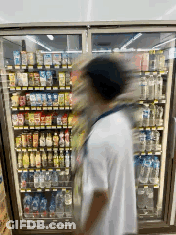 A Person Is Standing In Front Of A Refrigerator In A Store GIF