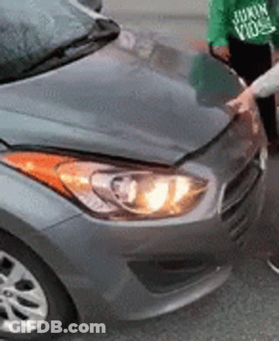 A Person Is Standing Next To A Gray Car With The Hood Up . GIF