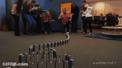 A Person Is Standing Next To A Row Of Dominoes In A Hallway . GIF