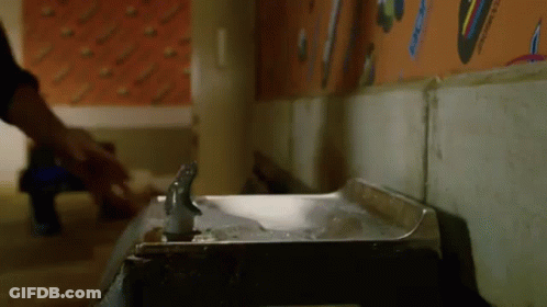 A Person Is Standing Next To A Water Fountain In A Room . GIF