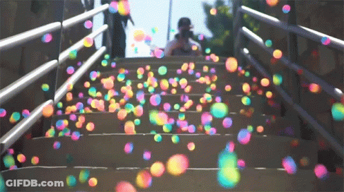 A Person Is Standing On A Set Of Stairs Surrounded By Colorful Soap Bubbles GIF