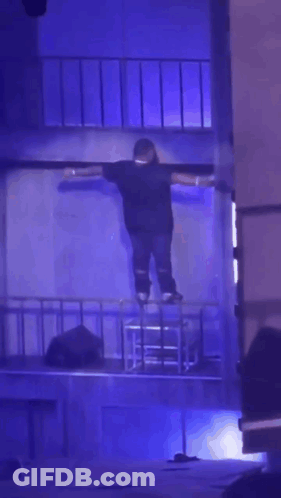 A Person Is Standing On A Stage With Their Arms Outstretched In A Dark Room GIF