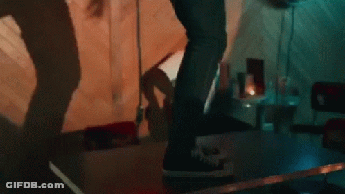 A Person Is Standing On A Table In A Dark Room With A Shadow On The Wall . GIF