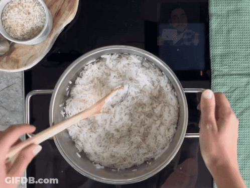 A Person Is Stirring A Pot Of Rice With A Wooden Spoon GIF