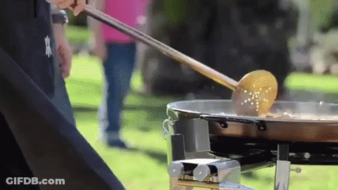 A Person Is Stirring Food In A Pan With A Wooden Ladle GIF