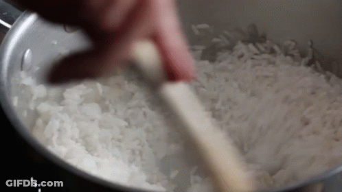 A Person Is Stirring Rice With A Wooden Spoon In A Pot . GIF