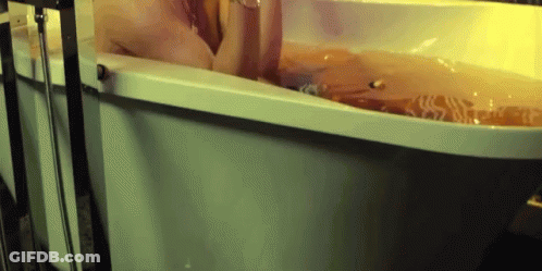 A Person Is Taking A Bath In A Bathtub Filled With Water . GIF
