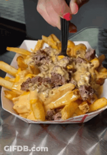 A Person Is Taking A Bite Of French Fries With Cheese GIF