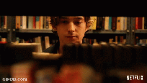 A Person Is Taking A Book Out Of A Bookshelf With A Netflix Logo In The Corner GIF