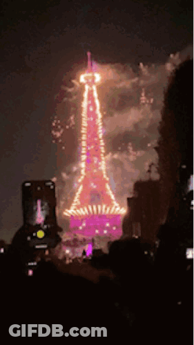 A Person Is Taking A Picture Of A Tower Lit Up At Night GIF