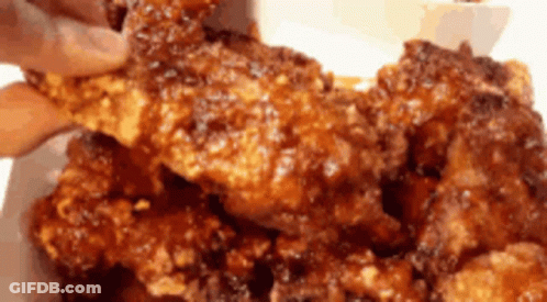 A Person Is Taking A Piece Of Fried Chicken From A Plate GIF