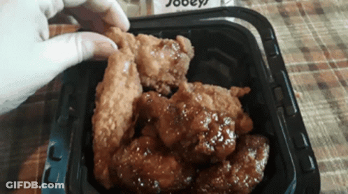 A Person Is Taking A Piece Of Fried Chicken Out Of A Container GIF