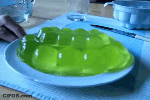 A Person Is Taking A Piece Of Green Jelly From A White Plate GIF