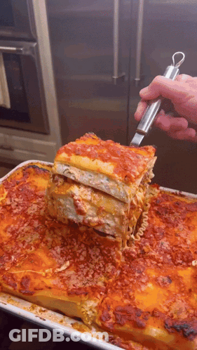 A Person Is Taking A Slice Of Lasagna From A Pan GIF