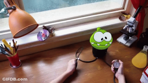 A Person Is Taking Their Blood Pressure With A Green Cartoon Character On The Desk GIF