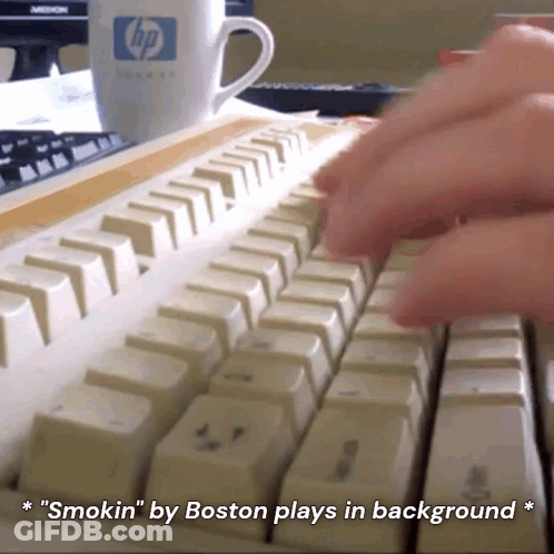 A Person Is Typing On A Keyboard With A Cup Of Coffee In The Background GIF